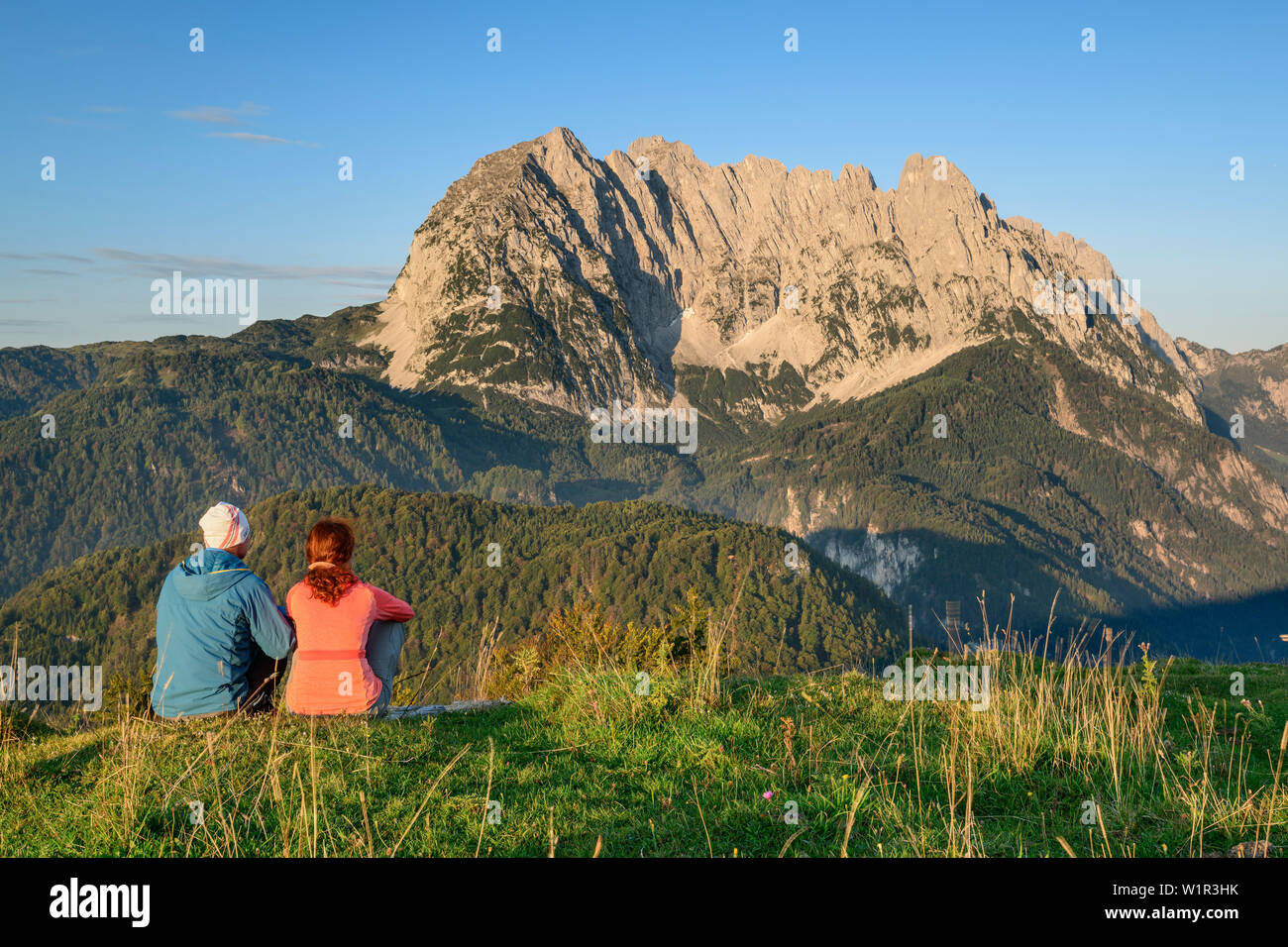 Ein Mann und eine Frau sitzt auf der Wiese und Blick auf den Wilden Kaiser, in der Morgendämmerung, hinter Wilder Kaiser, Kaisergebirge, Tirol, Österreich Stockfoto