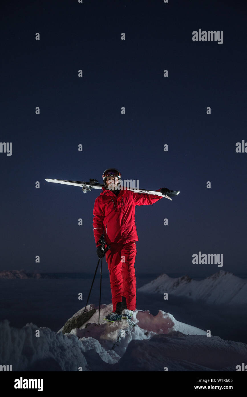 Junge männliche Skifahrer stehen auf der Spitze eines Berges über den Wolken bei Nacht, Kaprun, Salzburg, Österreich Stockfoto