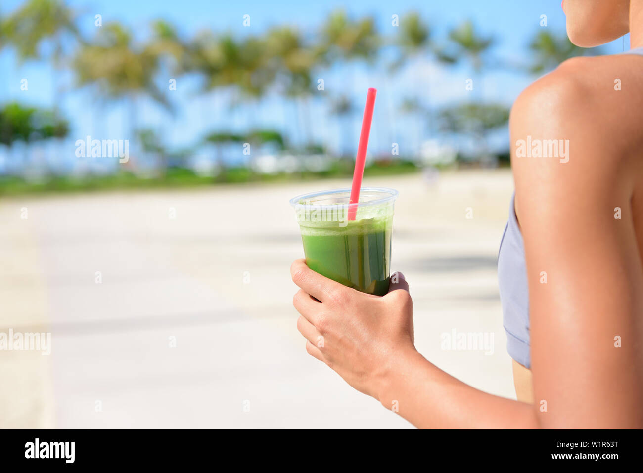 Pflanzliche grün Detox-smoothie reinigen - Frau trinkt nach Fitness Lauftraining auf Sommertag. Mädchen trinken grünen Saft oder Smoothie in Fitness und gesunde Lebensweise. Schöne Passform gemischten Rennen asiatischen Kaukasischen Modell außerhalb am Strand. Stockfoto