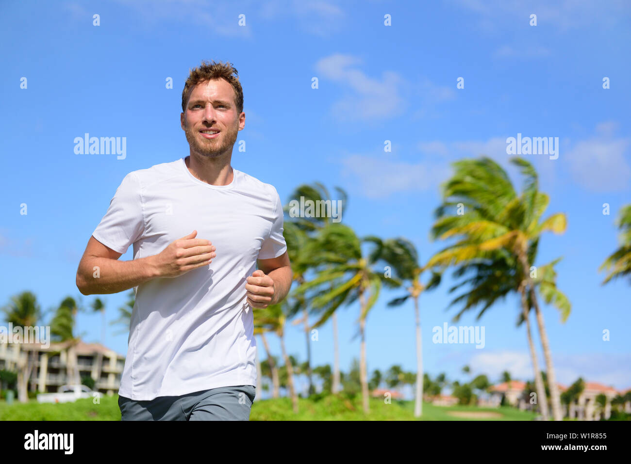 Gesunden aktiven Mann Runner im tropischen Park läuft. Portrait von gutaussehenden jungen männlichen Jogger training cardio gehen für einen Lauf im Stadtpark oder Resort mit Palmen im Hintergrund im Sommer. Stockfoto