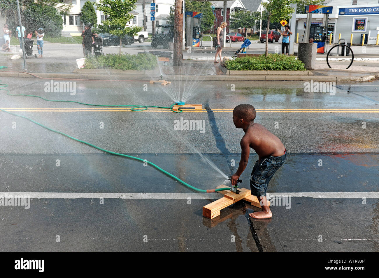 Ein junger schwarzer Junge leitet eine Sprinkleranlage während einer Hitzewelle in der collinwood Nachbarschaft von Cleveland, Ohio, USA. Stockfoto