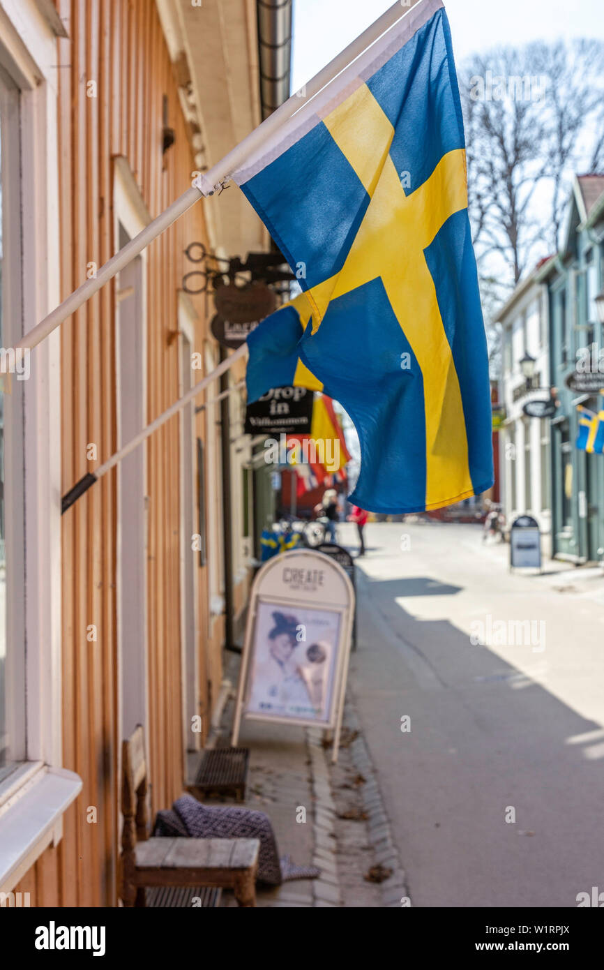Blau und gelb gefärbte nationale schwedische Flagge hängt außerhalb der ein Geschäft auf der Hauptstraße in Sigtuna, Schweden... die älteste Stadt in Schweden. Stockfoto
