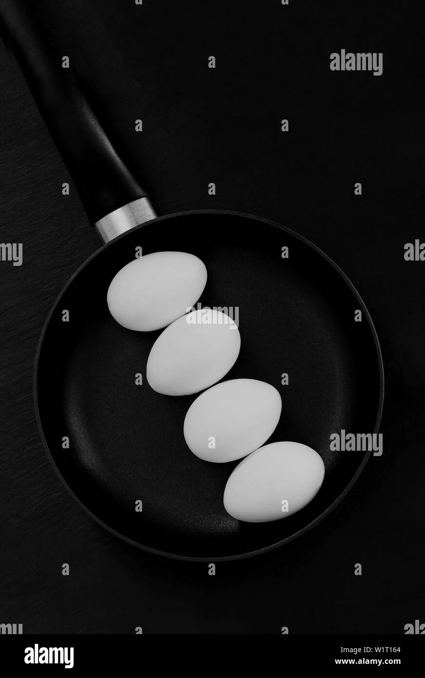 Vier weiße rohe Eier in der Schale liegen auf einem Schwarz Bratpfanne, stehend auf einem schwarzen Hintergrund bereit für Frühstück Stockfoto