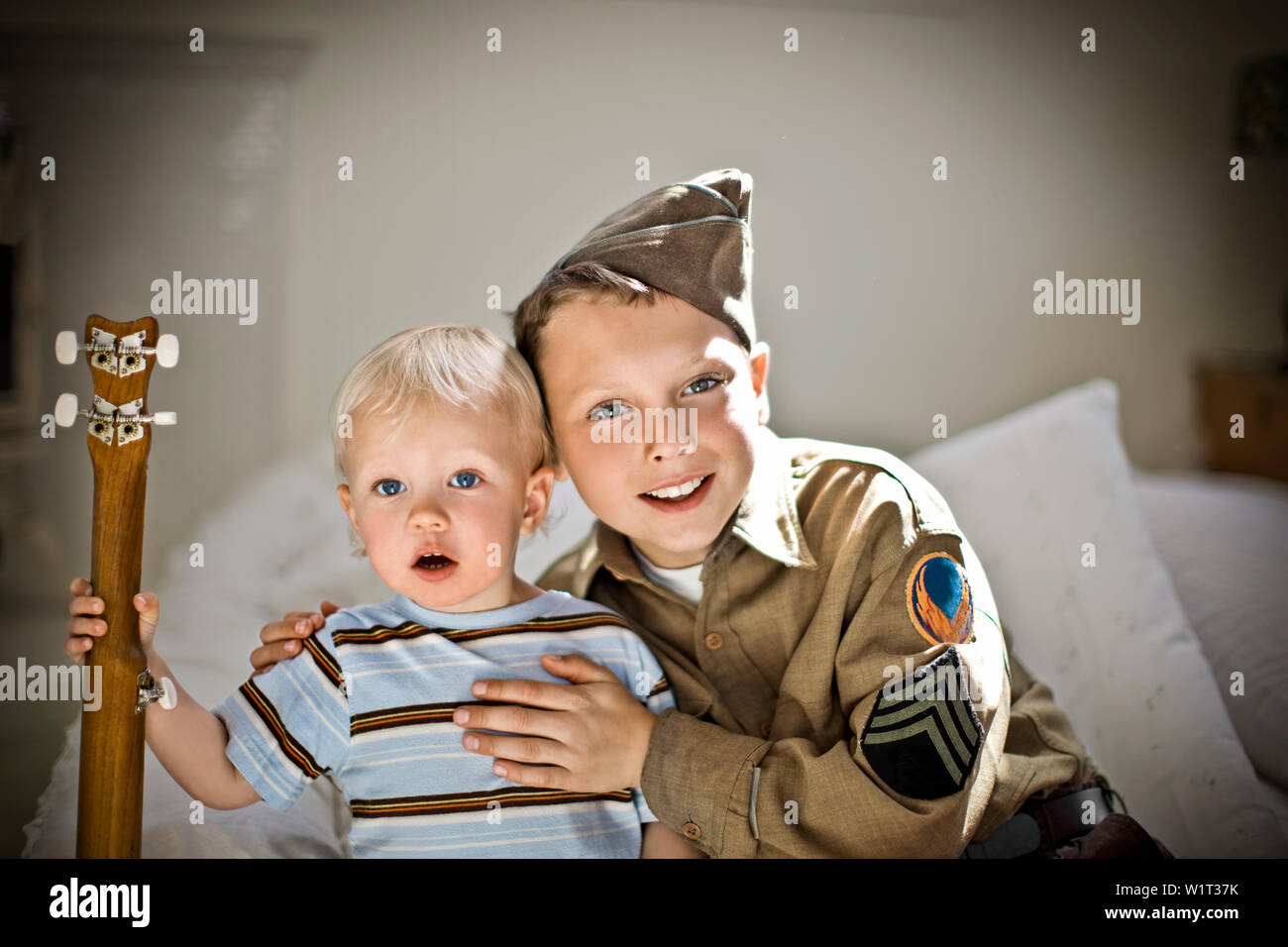 Porträt eines lächelnden Junge sitzt mit seinen Arm um seinen Bruder beim Tragen eines Soldaten uniform. Stockfoto