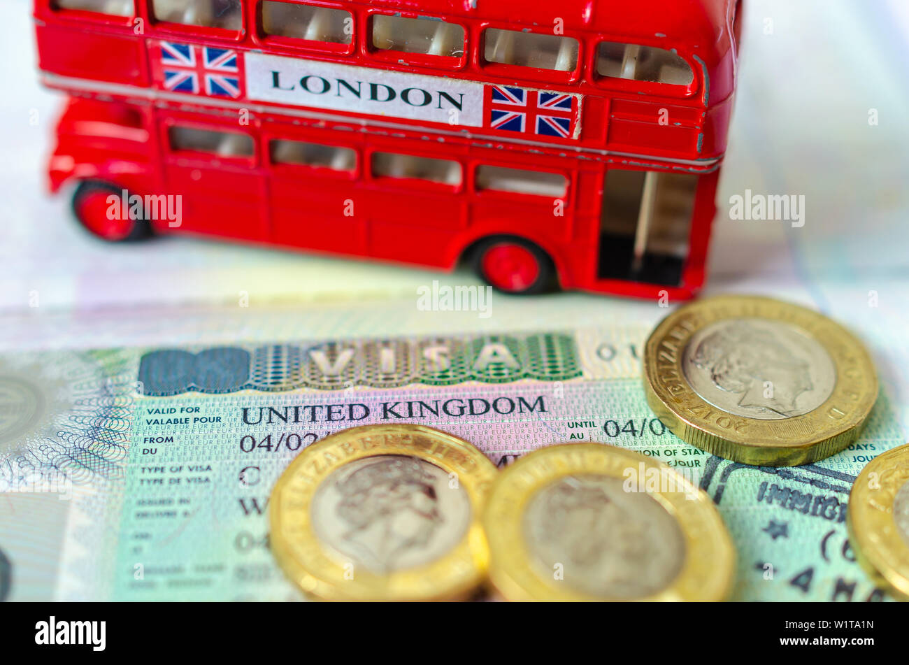 UK Visa Aufkleber in einem Paß von Pfund Münzen und Doppeldecker Bus Modell umgeben. Konzept für Reisen und Urlaub. Stockfoto