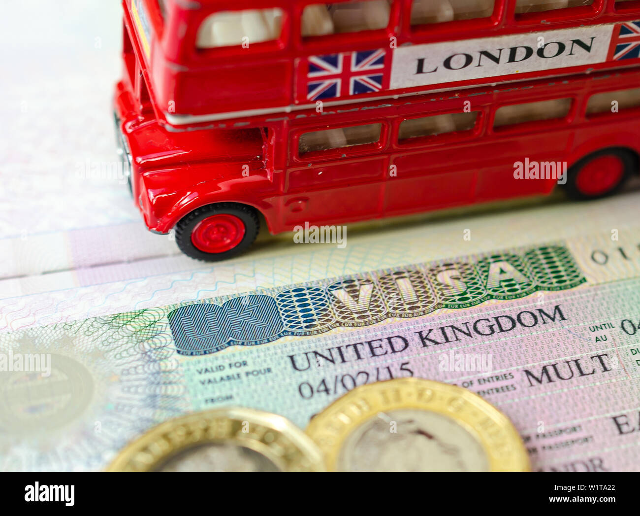 UK Visa Aufkleber in einem Paß von Pfund Münzen und Doppeldecker Bus Modell umgeben. Konzept für Reisen und Urlaub. Stockfoto