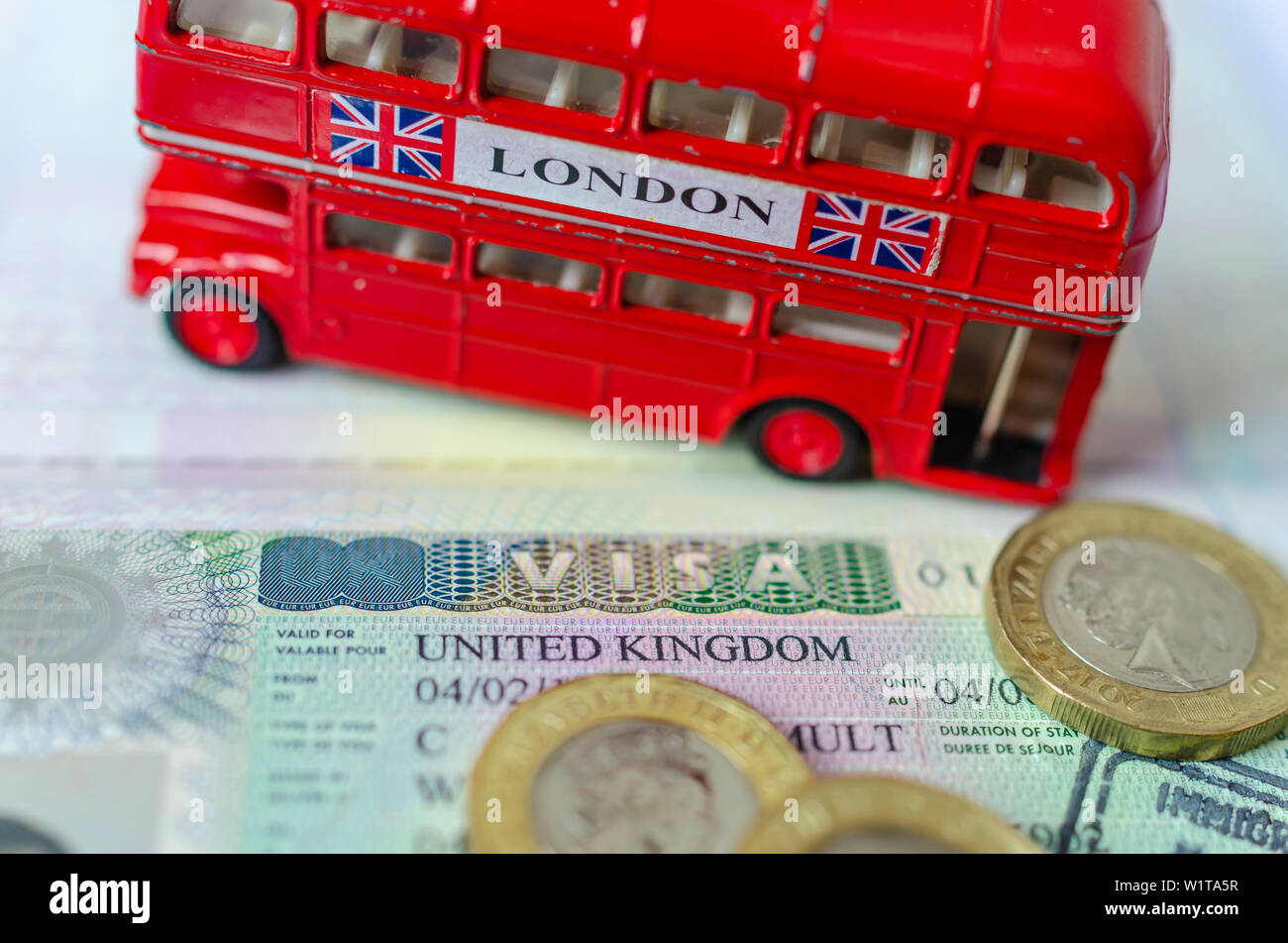 UK Visa Aufkleber in einem Paß von Pfund Münzen und Doppeldecker Bus Modell umgeben. Konzept für Reisen und Urlaub. Stockfoto