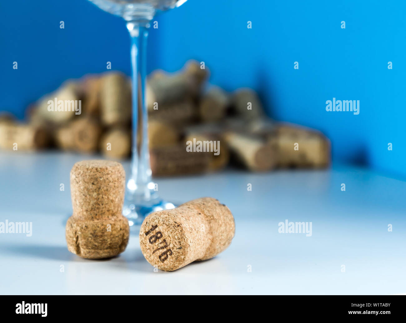 Ein leeres Weinglas auf blauem Hintergrund steht auf einem weißen Tisch. Korken von Weinflaschen. Verkostung teuren Wein. Stockfoto