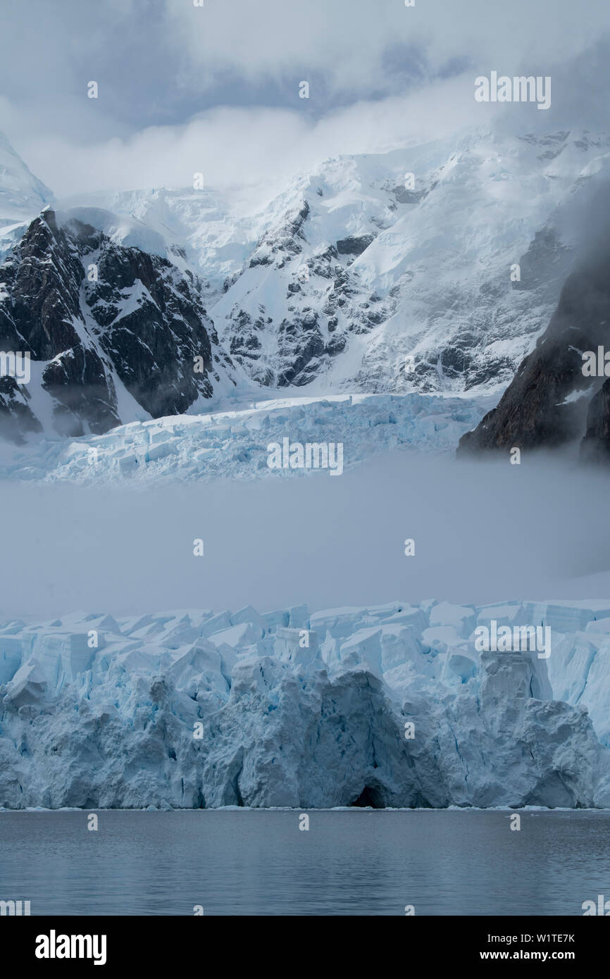 Nebel Schnitte durch die Mitte eines Gletschers durch Berge und Wolken gekrönt, Paradise Bay (Paradise Harbour), Danco Coast, Graham Land, Antarktis Stockfoto