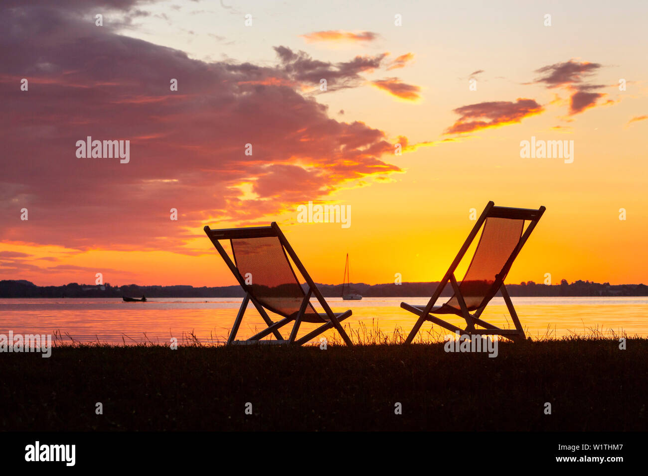 Zwei Sonnenliegen und Boote im letzten Abendlicht am Chiemsee Strand in Epenwöhrden Stockfoto