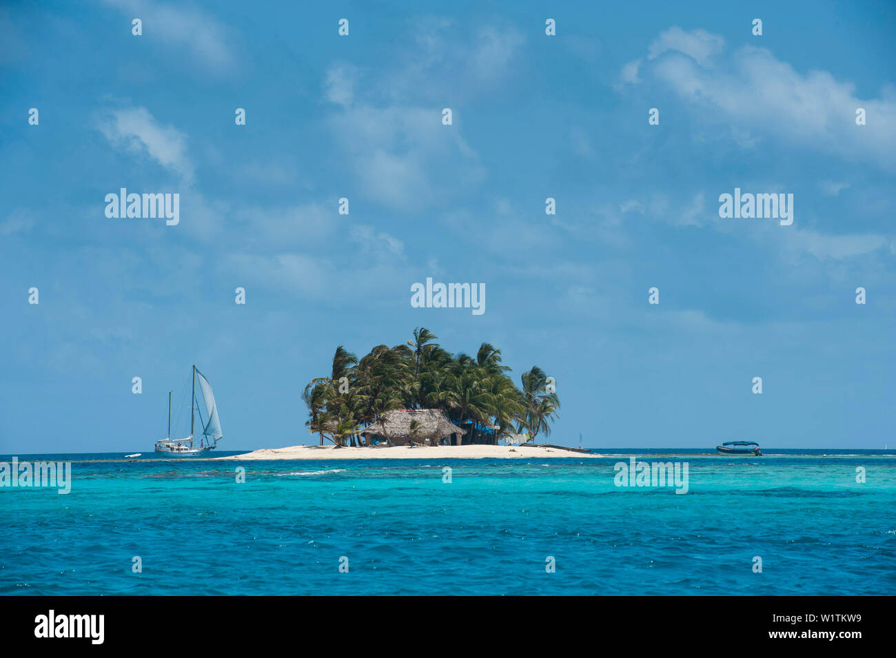 Blick auf eine Insel, die nur groß genug für eine Hütte und ein paar Dutzend Palmen, von einem Segelboot angefahren und flankiert auf der rechten Seite durch ein kleines Motorboot, Stockfoto