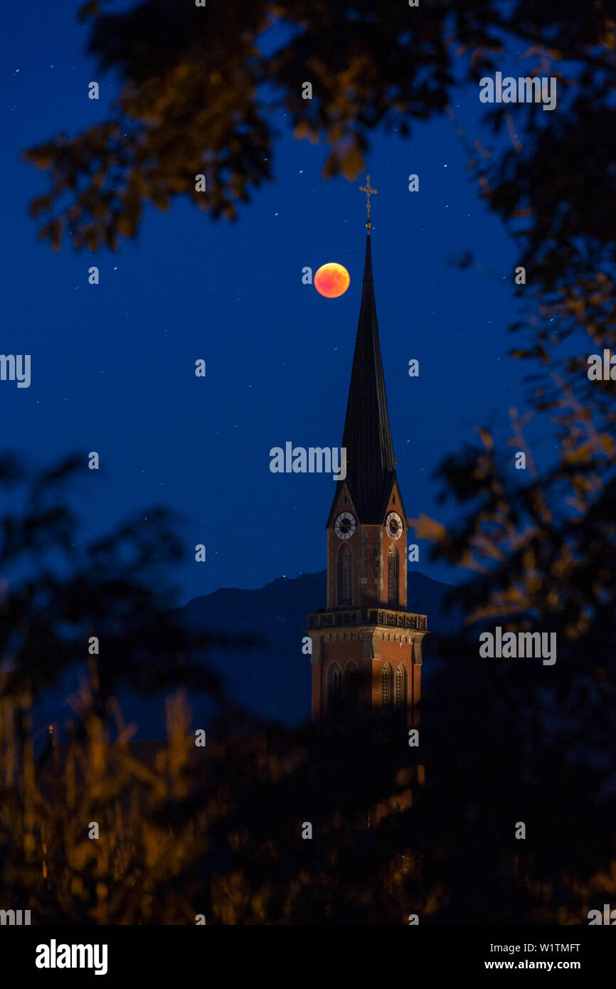 Blood Red Moon auf der Höhe der Mondfinsternis 2018; im Vordergrund die Pfarrkirche St. Nikolaus in Übersee hinter einem Maisfeld Stockfoto