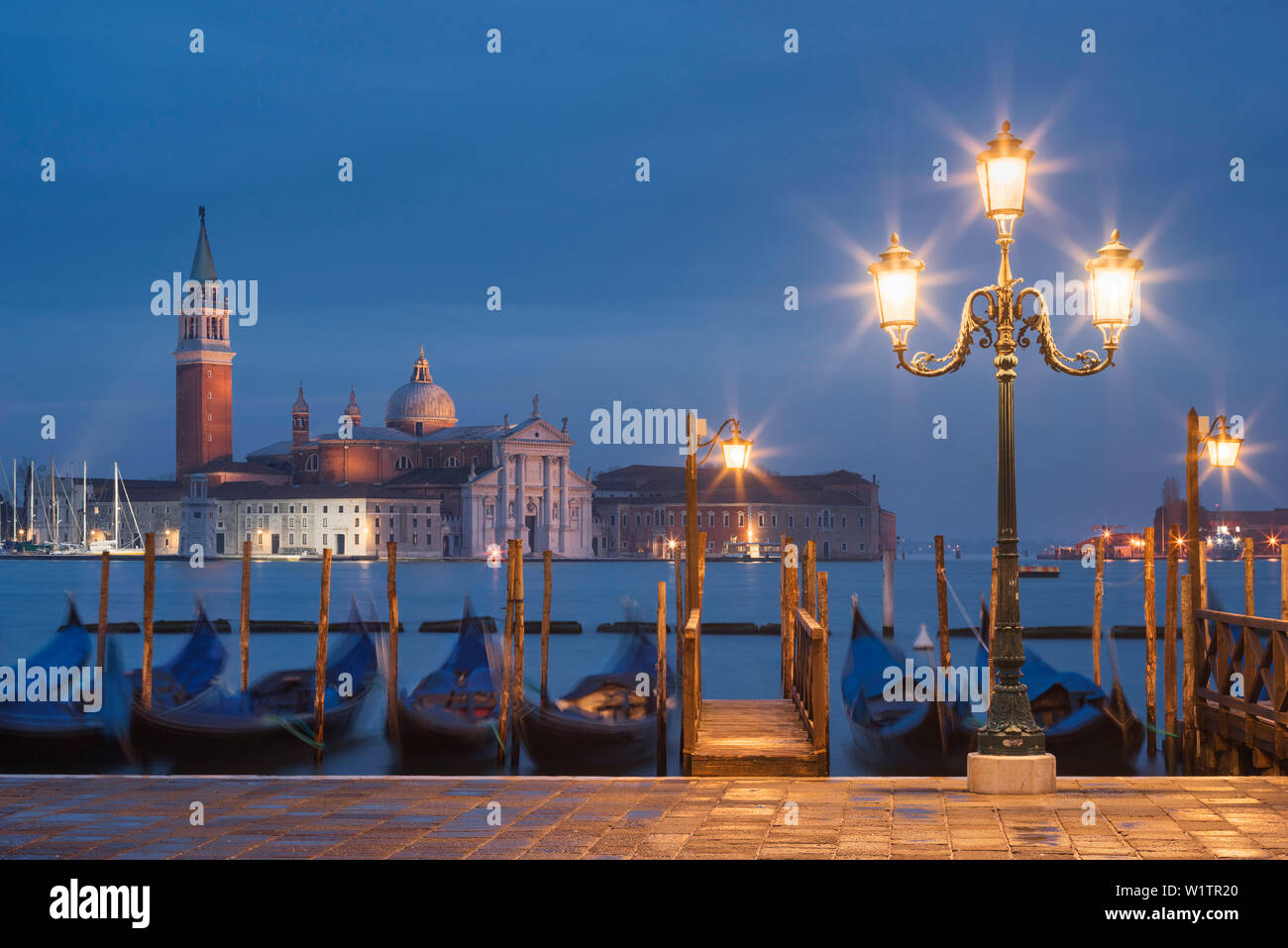 Blick vom St. Mark's Square mit Gondeln und Laternen auf die Insel San Giorgio Maggiore mit seinen Namensvetter Kirche in das Blau der Nacht, San Ma Stockfoto