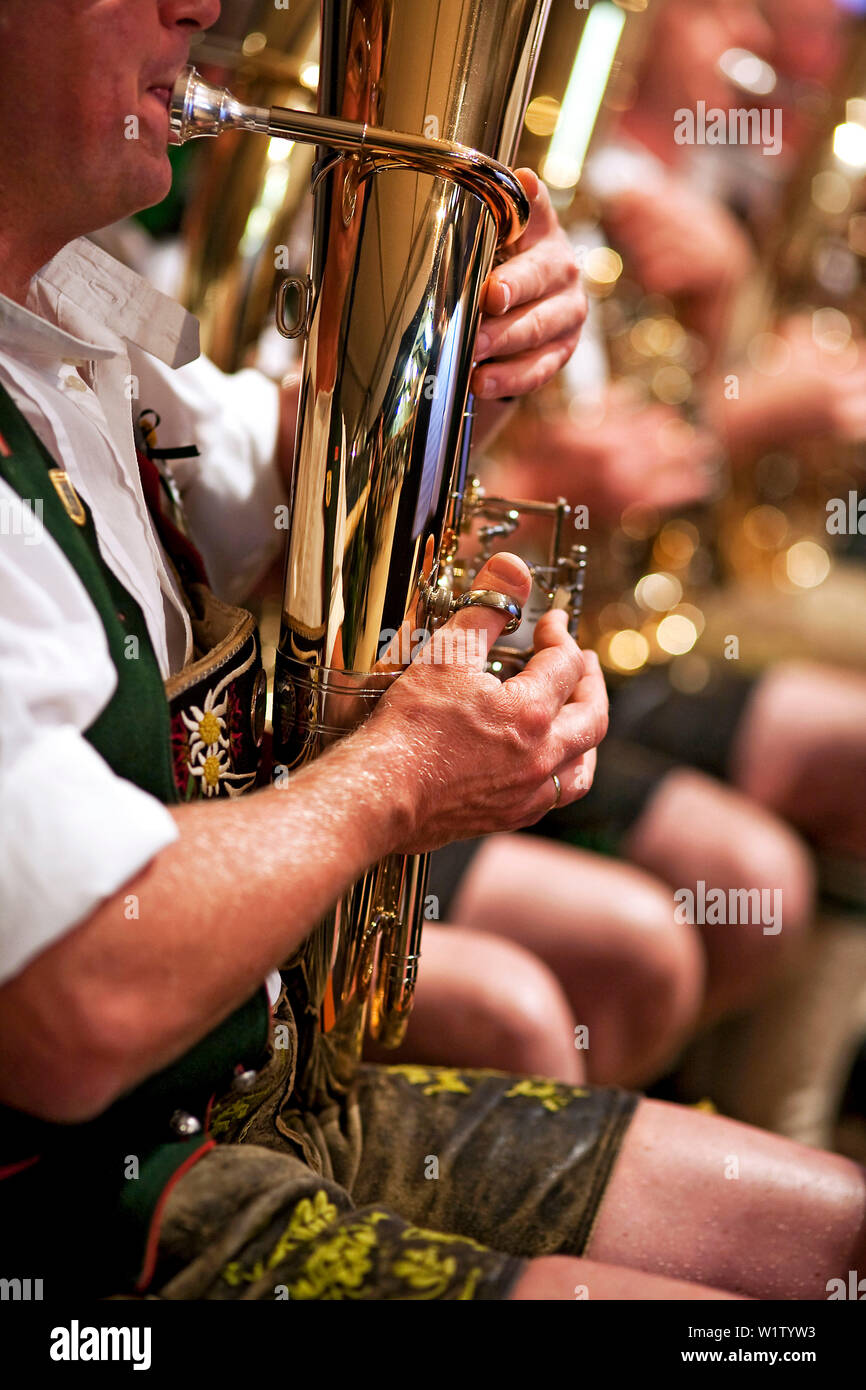 Musiker in bayerischer Tracht spielt Tenorhorn; weitere Musiker unscharf im Hintergrund; im Detail Stockfoto