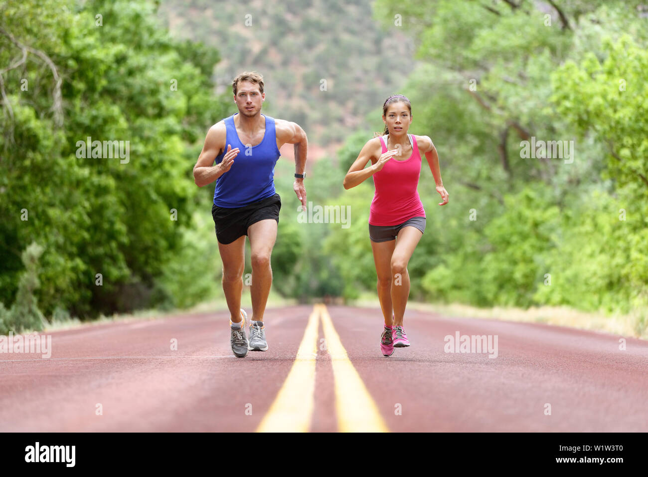 Bestimmt der Mann und die Frau, die auf der Straße gegen Bäume. Läufer sprintete in voller Länge sportlich männlich und weiblich sind in Sportbekleidung. Sportliche Läufer Fitness Sport paar Training unter. Stockfoto