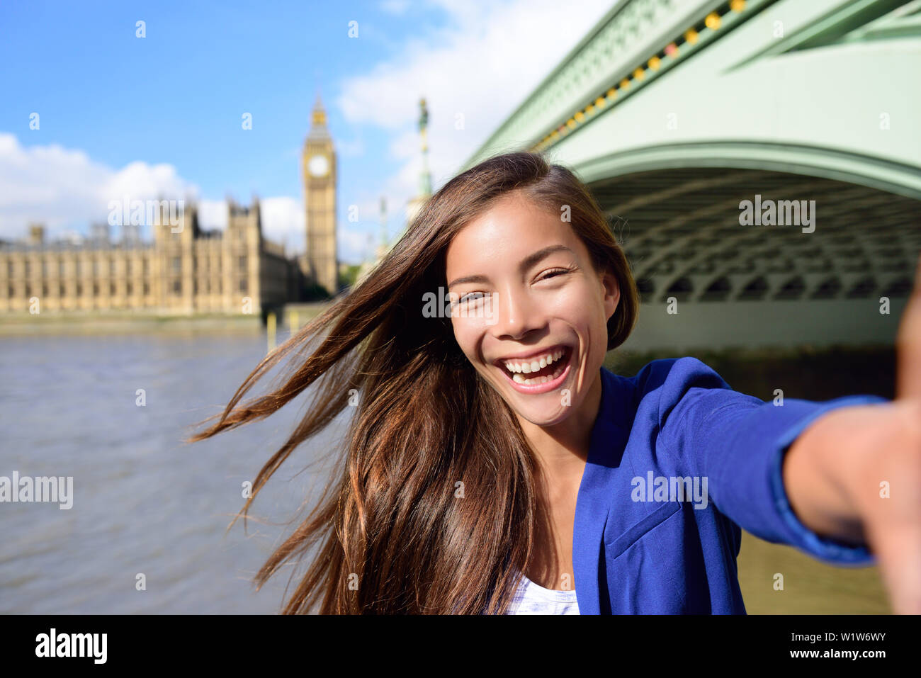 London reisen selfie Geschäftsfrau. Freudige junge Casual business Frau an der Kamera mit Thames River lächelnd, Big Ben und der Westminster Bridge im Hintergrund. Asiatische Tourist können Sie über Smartphone für Bild. Stockfoto