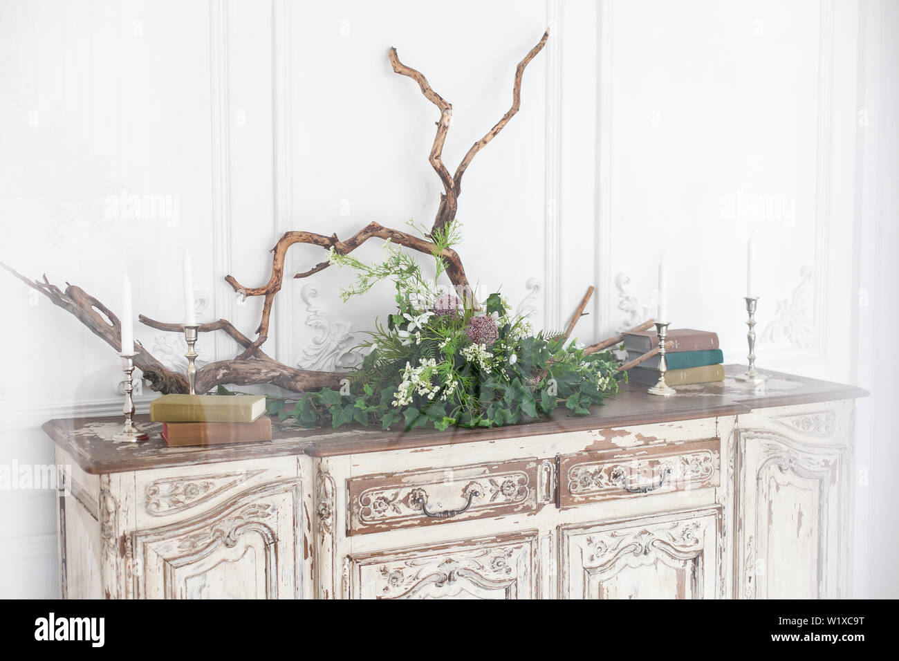 Die alte Rokoko Kommode ist mit Büchern, Kerzen, Treibholz und Pflanzen gegen die Wand mit Stuck verziert. Stockfoto