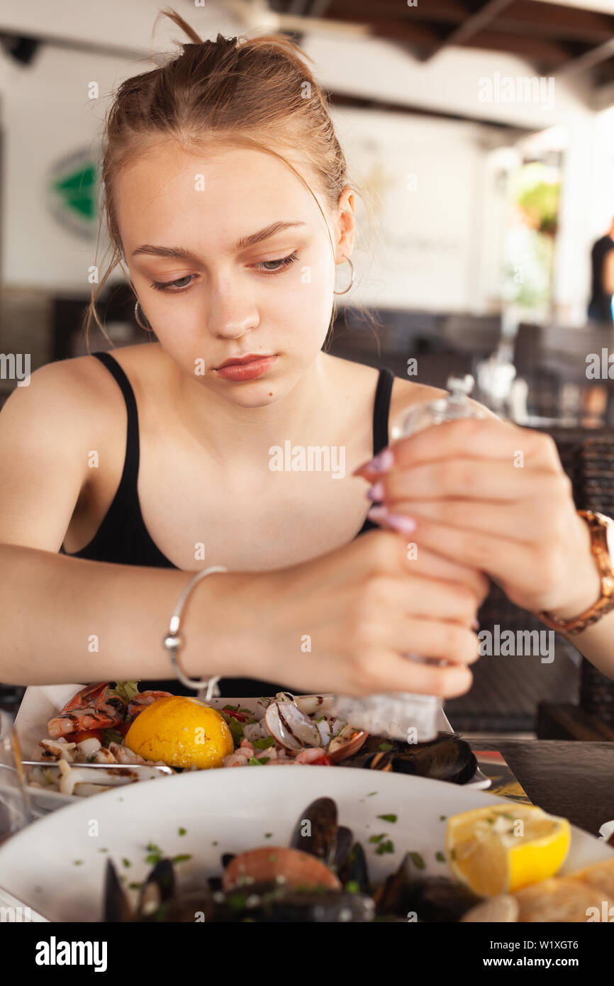 Junge schöne Blondine kaukasische Mädchen fügt Pfeffer in gemischten Salat mit Meeresfrüchten Stockfoto
