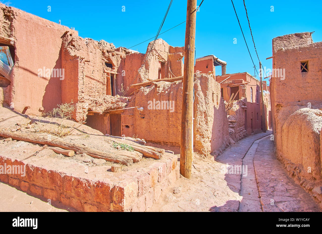 Die schmale Straße mit alten, verlassenen Gebäuden gesäumt und restaurierte Wohn häuser aus rotem Adobe, Abyaneh, Iran. Stockfoto