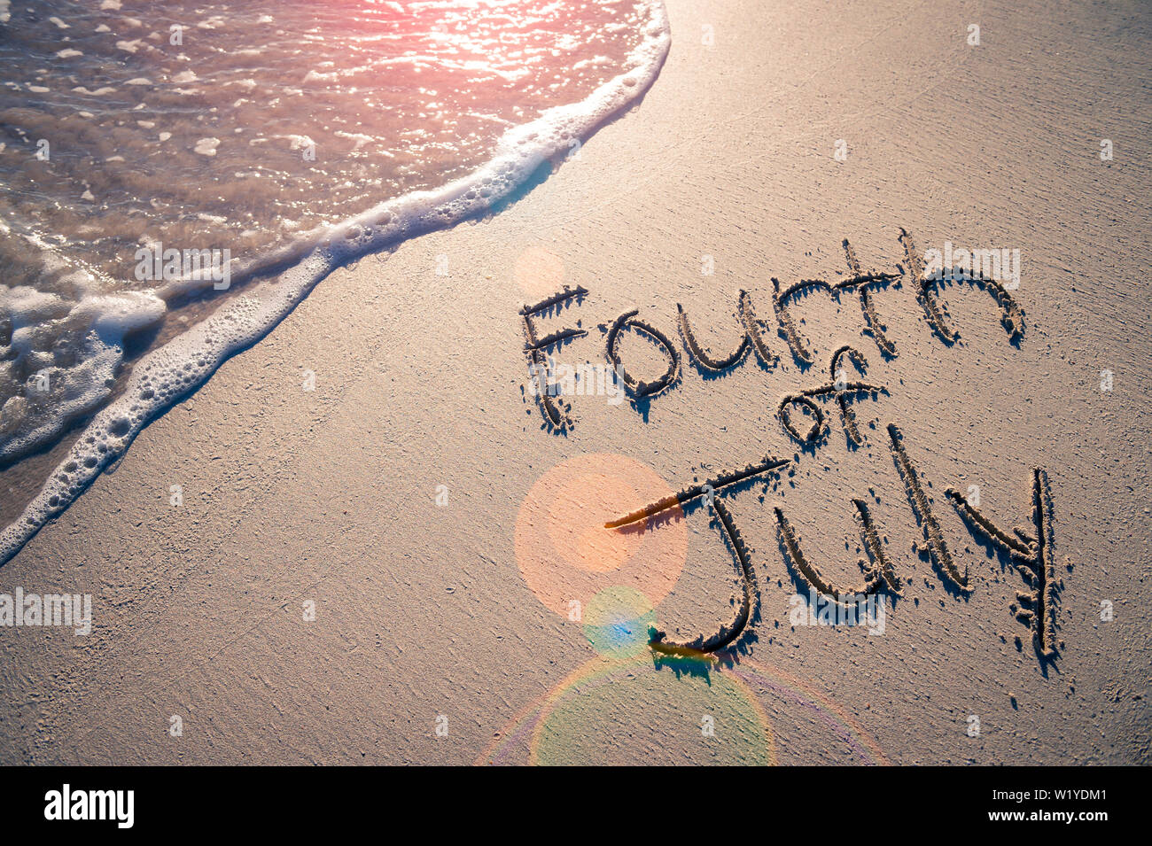 Am 4. Juli Nachricht für den amerikanischen Unabhängigkeitstag Urlaub in sanften Sand mit sonnigen lens flare Blick auf einen ankommenden Welle am Strand geschrieben Stockfoto