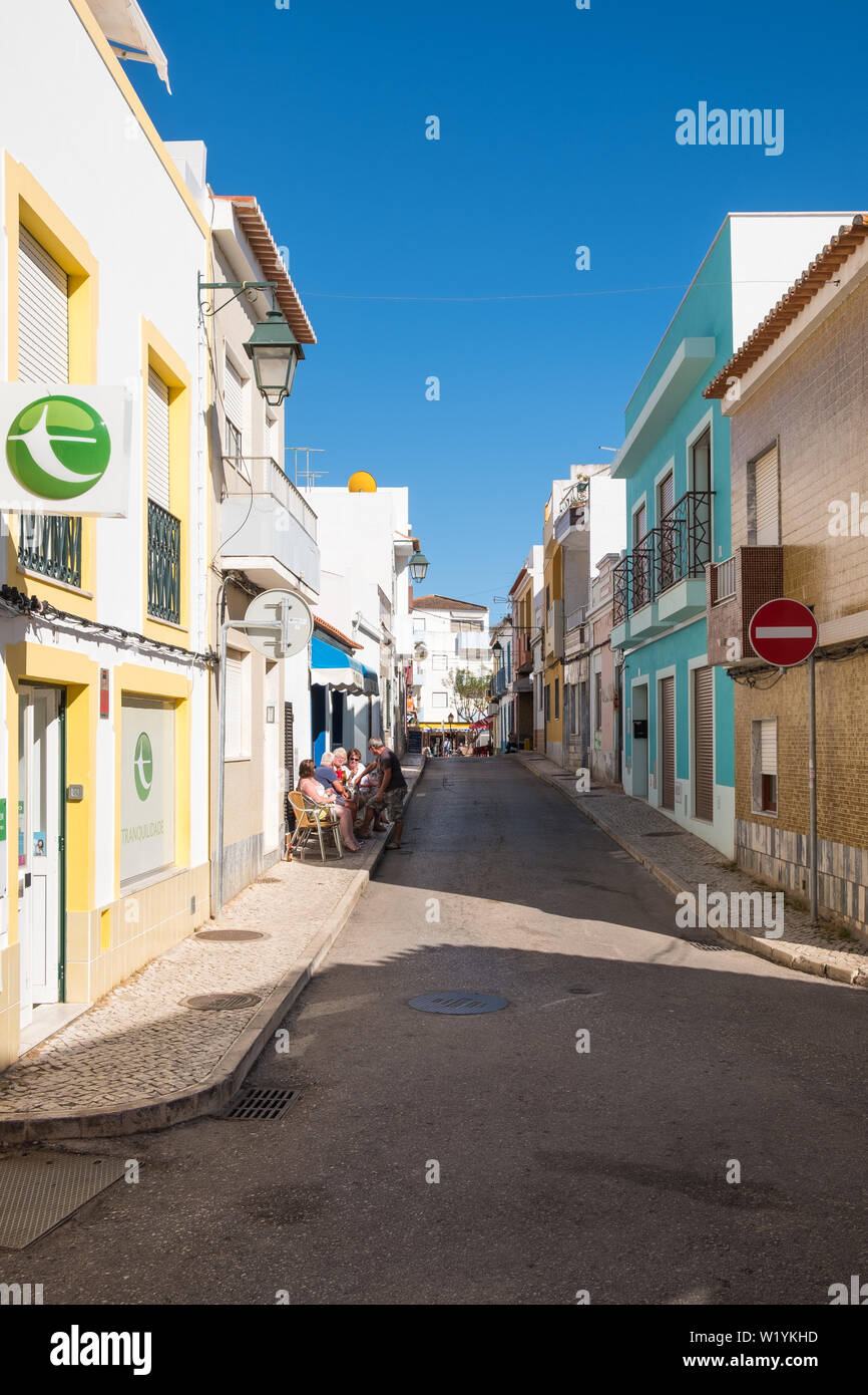 Schmale Straße mit Menschen sitzen draußen an der Bar in Alvor, Algarve, Portugal Stockfoto