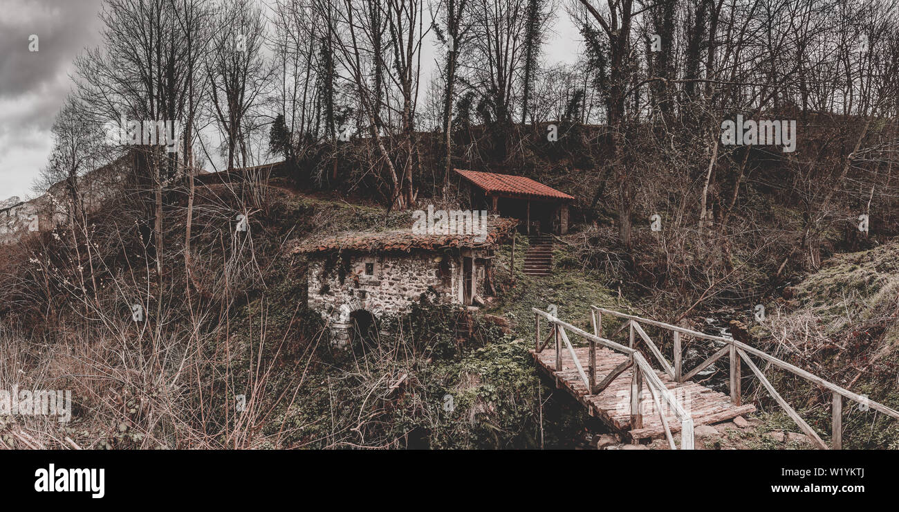 Panorama der alten Wassermühle in Viego, Asturien, Spanien. Im Vordergrund eine kleine Holzbrücke, die in der Mühle und Wald im Hintergrund führt Stockfoto