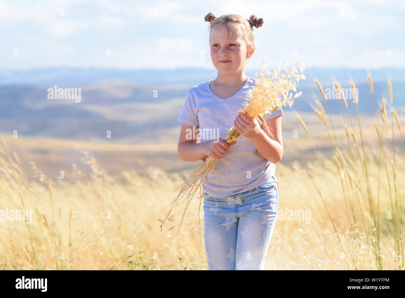 Gerne kleine Mädchen zu Fuß in goldenen Weizen, die Spikes von Weizen und Ohren von Hafer. Natur Schönheit, blauer Himmel, weiße Wolken und Feld von Weizen. Stockfoto