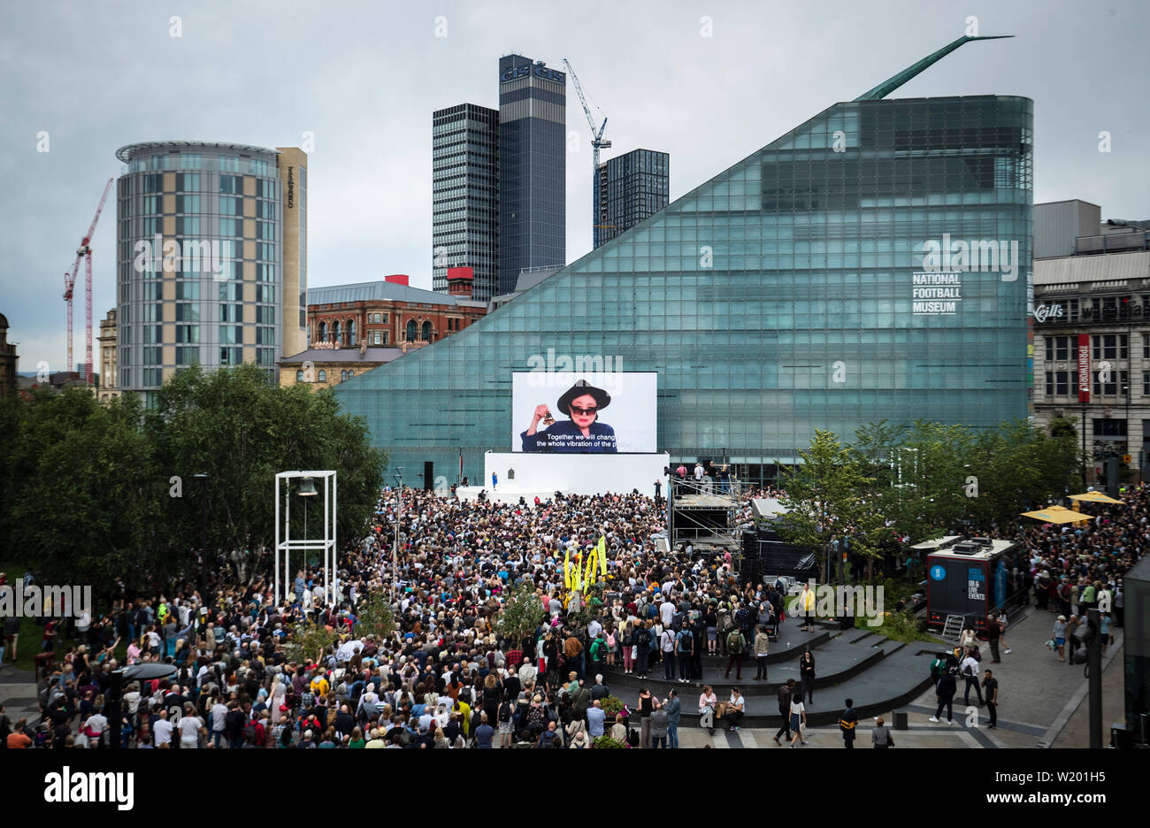 Tausende von Menschen kommen in Cathedral Gardens im Stadtzentrum von Manchester zusammen, um an einer einzigen partizipativen Kunstveranstaltung, GLOCKEN FOR PEACE, teilzunehmen, die von Yoko Ono entworfen und vom Manchester International Festival in Auftrag gegeben und produziert wurde. Stockfoto