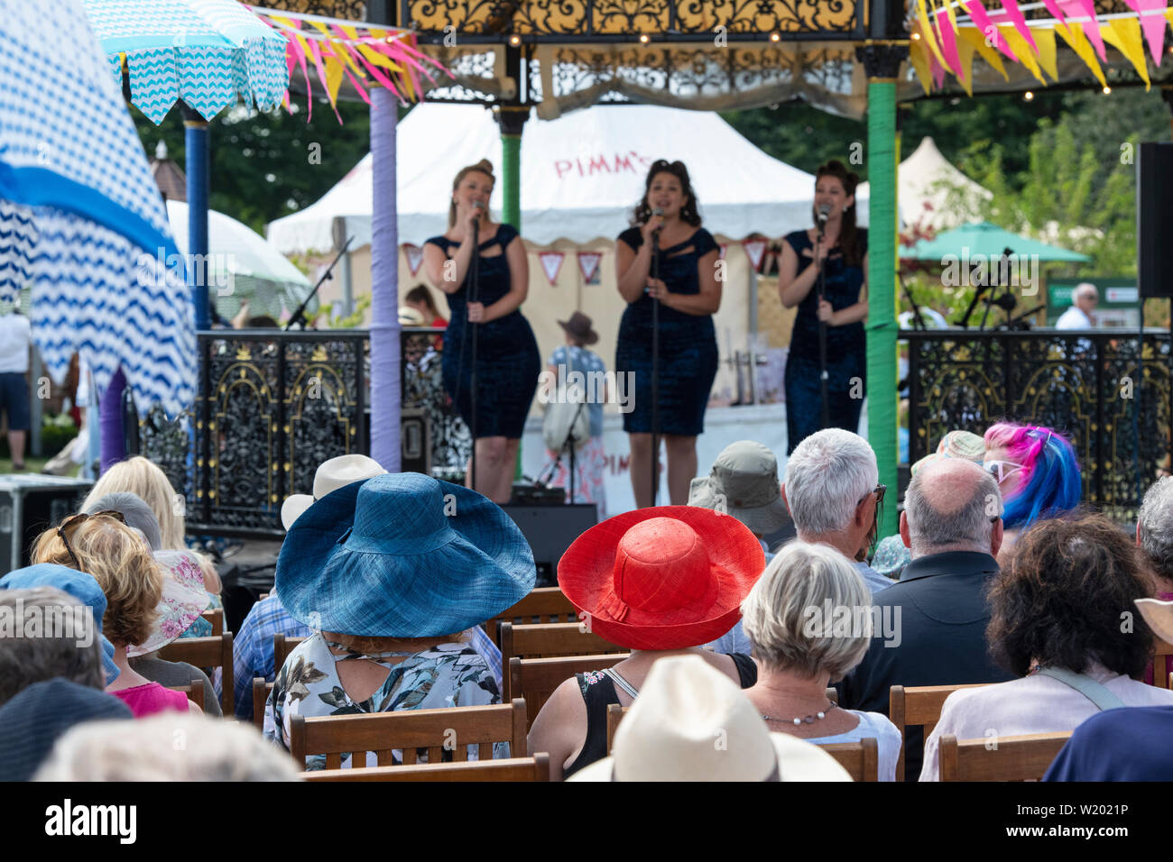 Leute saßen auf Stühlen, einen weiblichen Vintage boogie - woogie Gesangsgruppe im musikpavillon an der RHS Hampton Court Flower Show 2019. Surrey, England Stockfoto