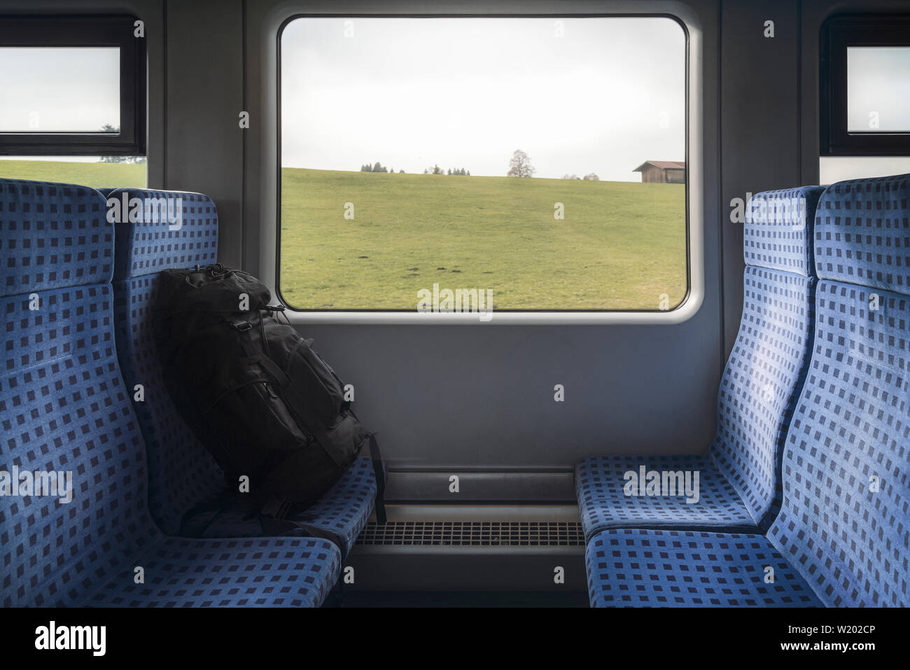 Reisen in Deutschland mit einem deutschen Regionalbahn Innenraum, blaue Stühle, schwarzer Rucksack, und Fenster mit Blick in die Natur. Stockfoto