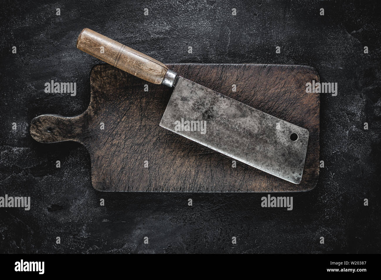 Rustikale Schneidbrett und Fleisch Cleaver auf dunklem Hintergrund. Metzgerei Werkzeug. Stockfoto