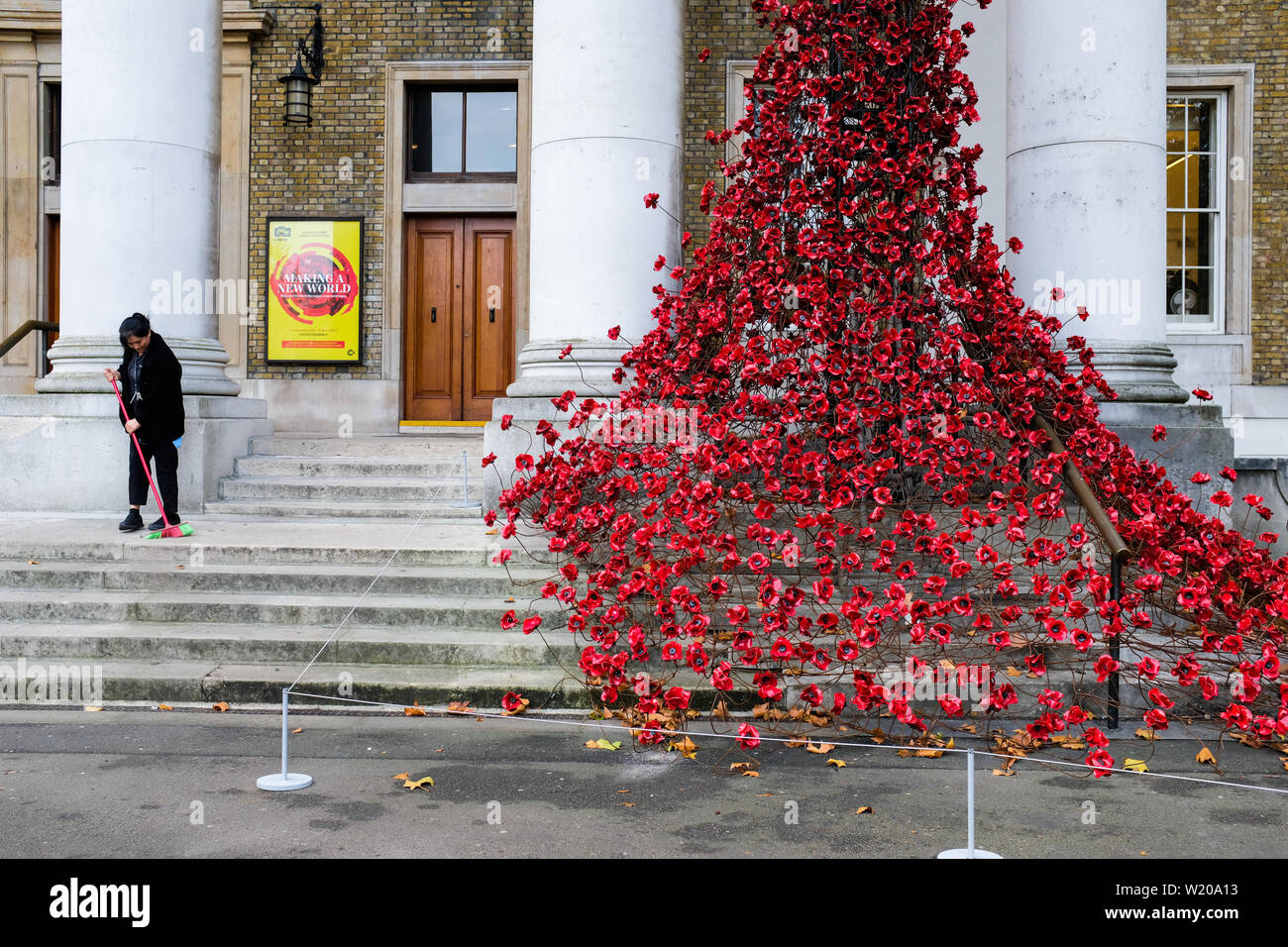 Mitarbeiter reinigt Eingang zum Imperial War Museum, London, in der Nähe der 100. Jahrestag der Armistice Day (2019) (daher der Mohnblumen). Stockfoto