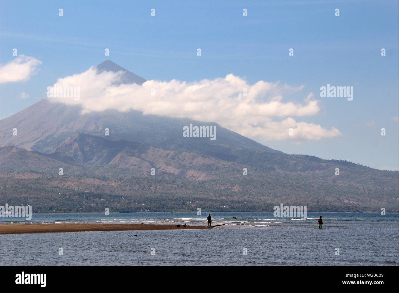 Fischer im Wasser eines Sees vor einem hohen Vulkan mit Wolken in Sulawesi, Indonesien. Stockfoto