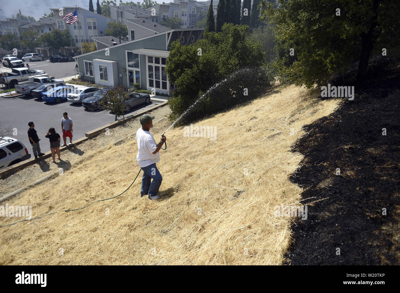 San Jose, CA, USA. 4. Juli 2019. San Jose, CA, USA - ein Hausbesitzer mit einem Gartenschlauch San Jose Feuerwehr Feuerwehrmänner zu helfen, kleine Flecken auf dem Hügel hinter seinem Haus. Der Brand auf dem Communications Hügel südlich der Innenstadt von San JosÃ © Mai bezogen worden sind, um eine Struktur zu Feuer in der Nähe. Credit: Neal Gewässer/ZUMA Draht/Alamy leben Nachrichten Stockfoto