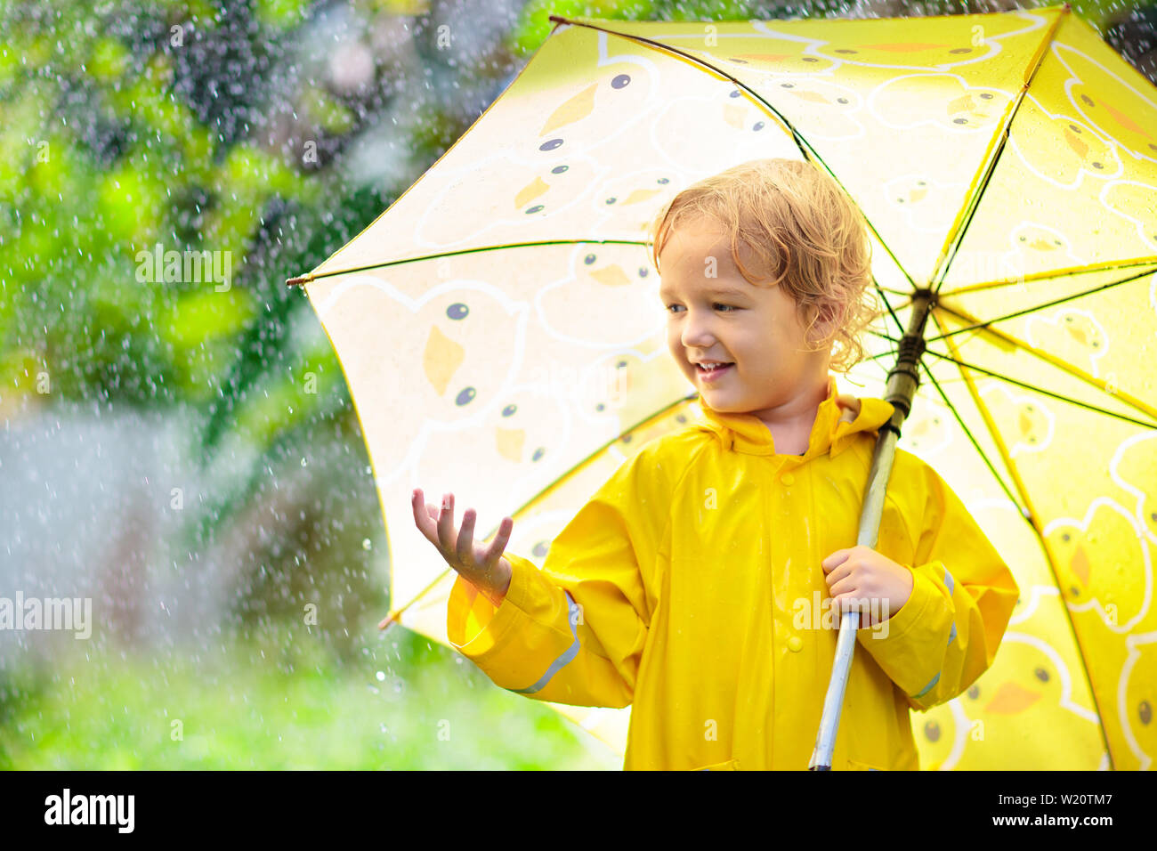 Kinder spielen im Regen an sonnigen Herbsttag. Kind unter schweren Dusche mit gelber Ente Regenschirm. Kleine Junge mit Entlein wasserdichte Schuhe. Gummi wel Stockfoto