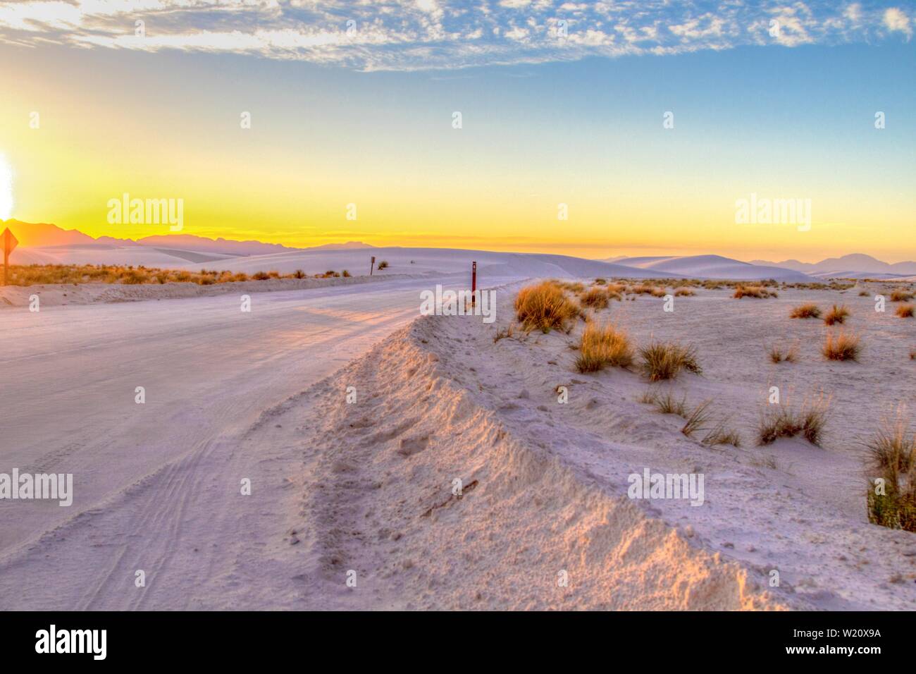 Road Trip In Die Wüste. Wunderschöner Sonnenuntergang in der Wüste mit abgelegener Landstraße, die sich durch die Sanddünen des White Sands National Monument in New Mexico schlängelt Stockfoto
