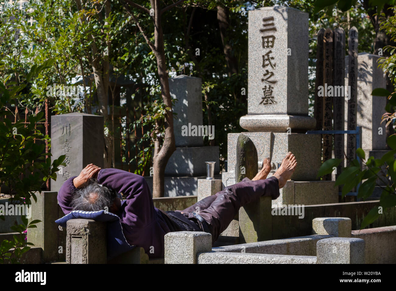 Ein Obdachloser schläft auf Grabsteinen auf einem Friedhof in Azabu, Tokio, Japan. Stockfoto