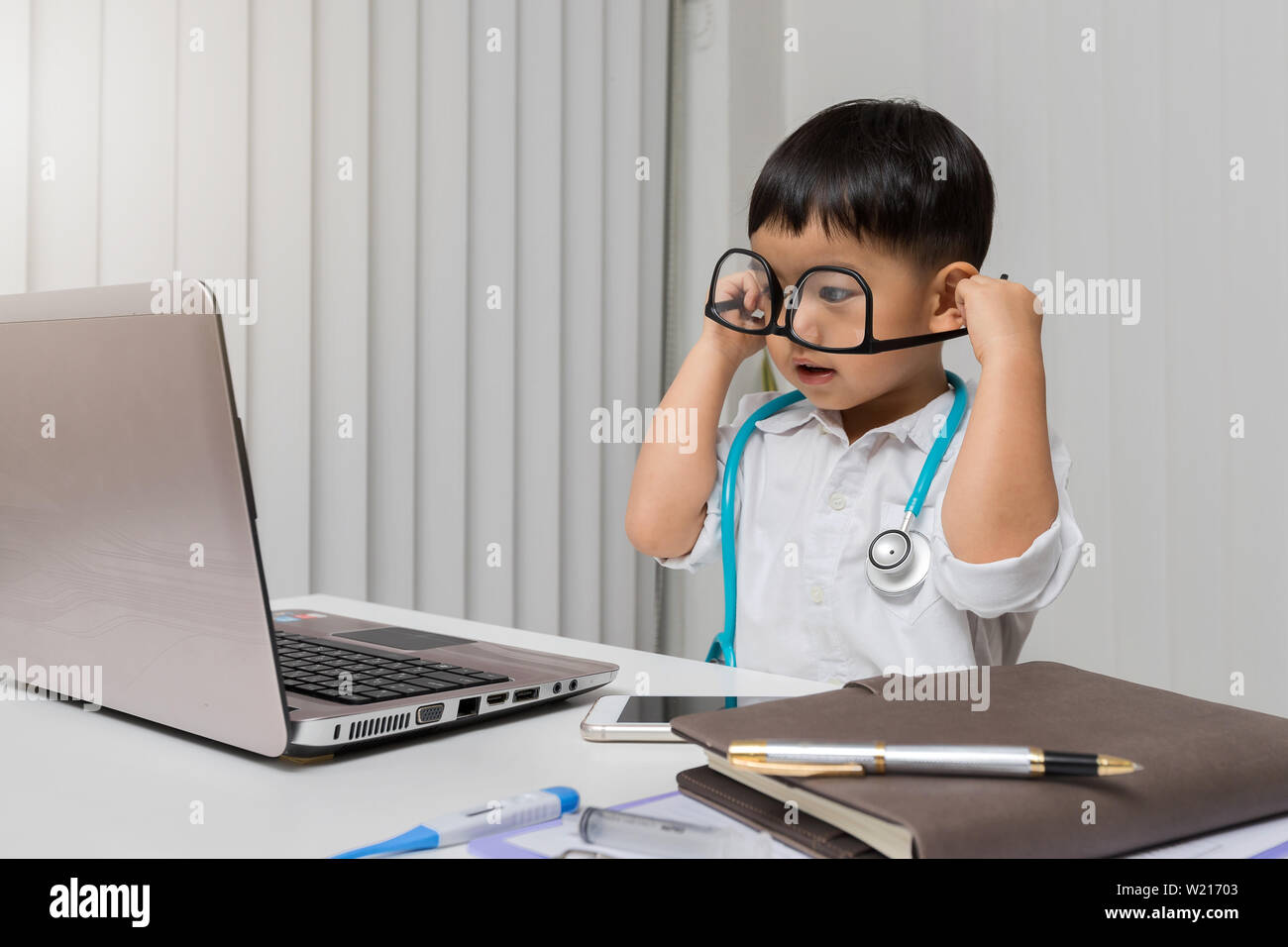 Little Boy in Medic einheitliche eine Brille trägt falsche Seite und am Laptop. Stockfoto