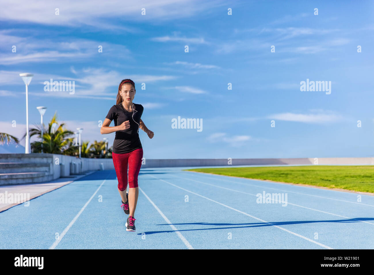 Weibliche asiatische Athleten runner auf blauen Titel im Freien Stadion läuft im Sommer. Sportliche Frau joggen Musik hören mit Kopfhörern training cardio für Gewichtverlust Erfolg. Wellness und Gesundheit. Stockfoto