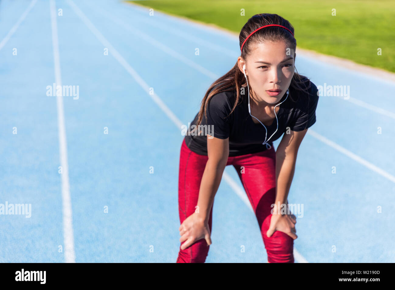 Läufer, die sich auf im Freien laufende Titel müde eine Pause, Entschlossenheit und Motivation bereit für die Herausforderung. Athlet Frau Musikhören mit Kopfhörern für konzentrieren. Stockfoto