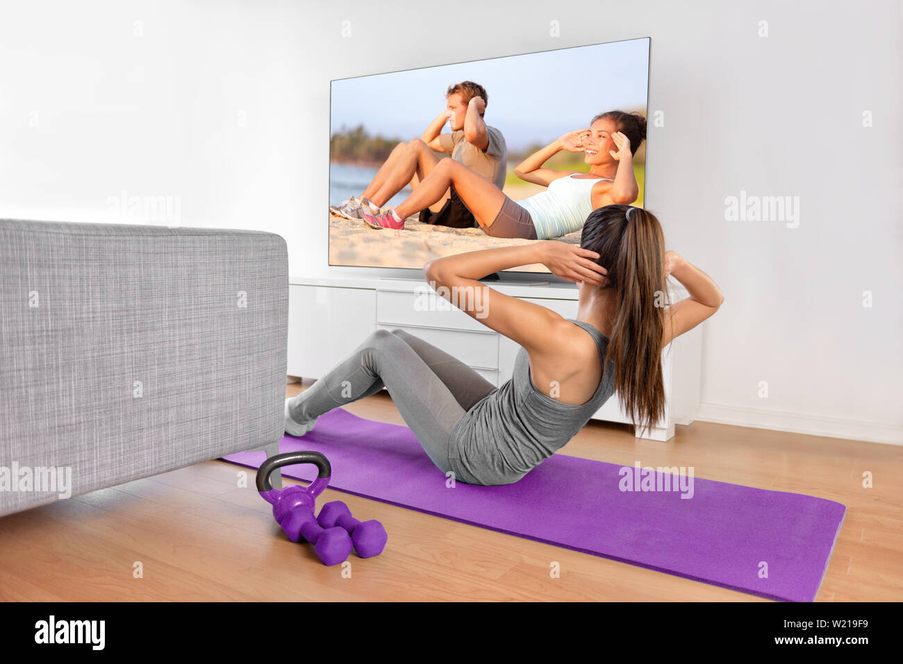 Home Training - Frau Ausübung vor einem Flachbildschirm mit einem fitnessprogramm oder Trainieren während einer TV-Show liegen auf einem Yoga Matte vor dem Sofa im Wohnzimmer eines Hauses oder einer Wohnung. Stockfoto