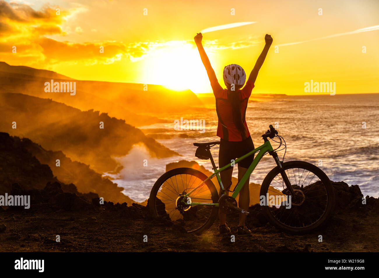 Erfolg, Verwirklichung, Vollendung und gewinnende Konzept mit Radfahrer Mountainbiken. Gewinnen glücklich MTB Frau Radfahren erreichen Ziel Anheben der Arme bei Sonnenuntergang Jubeln und Feiern auf dem Gipfel. Stockfoto