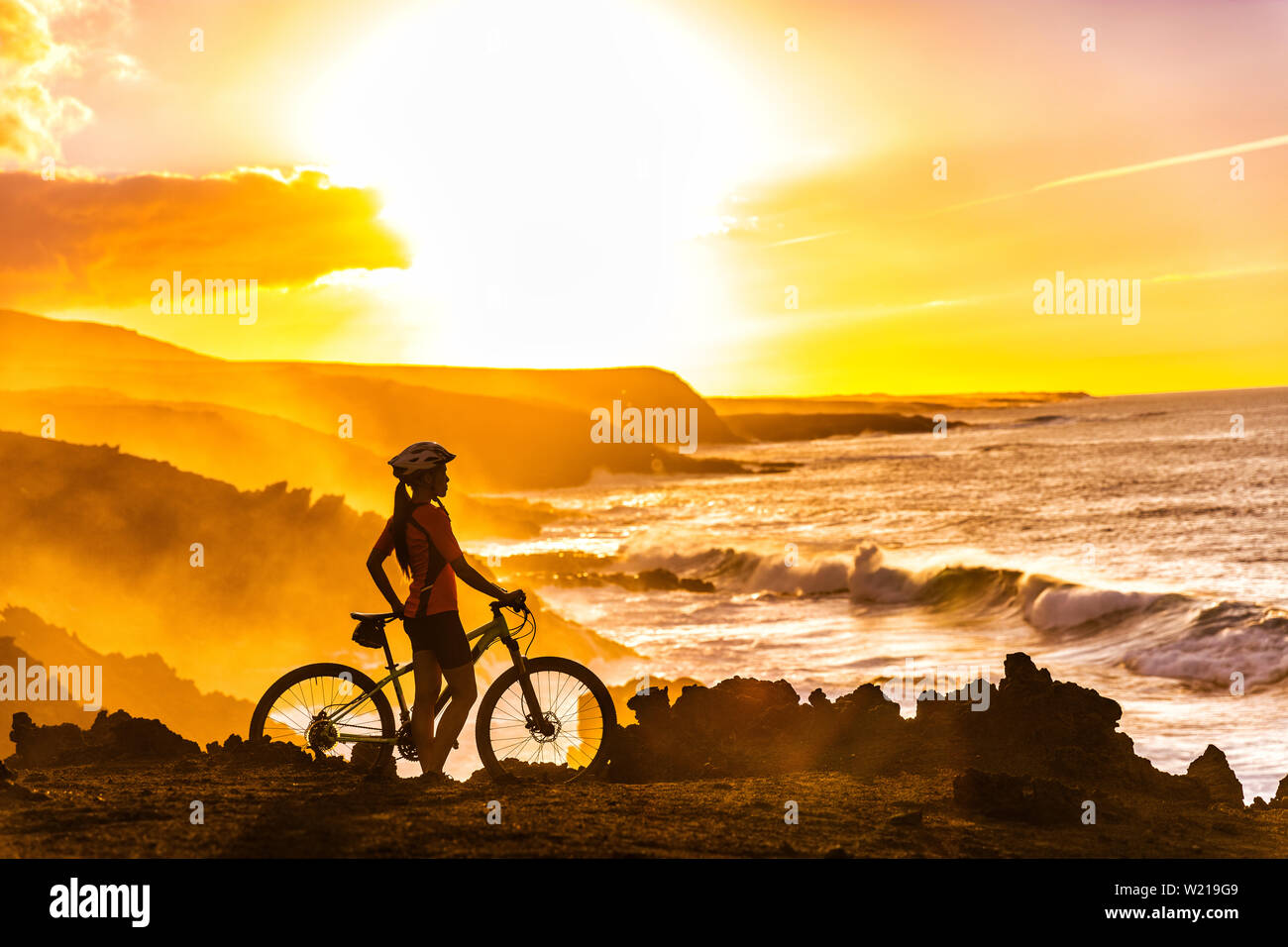 MTB Radfahrer Mountainbiken Frau Radfahren mit Blick auf den Radweg an der Küste bei Sonnenuntergang. Person auf dem Fahrrad durch Meer in Sportswear mit Fahrrad mit gesunden, aktiven Lebensstil in der wunderschönen Natur. Stockfoto