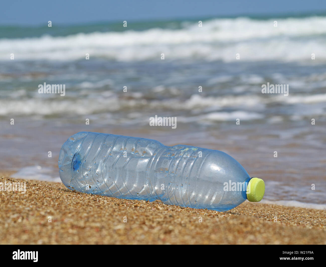 Kunststoff Flasche im Sand am Strand mit Wellen im Hintergrund, Konzept der Meeresverschmutzung durch Abfälle aus Kunststoffen Stockfoto