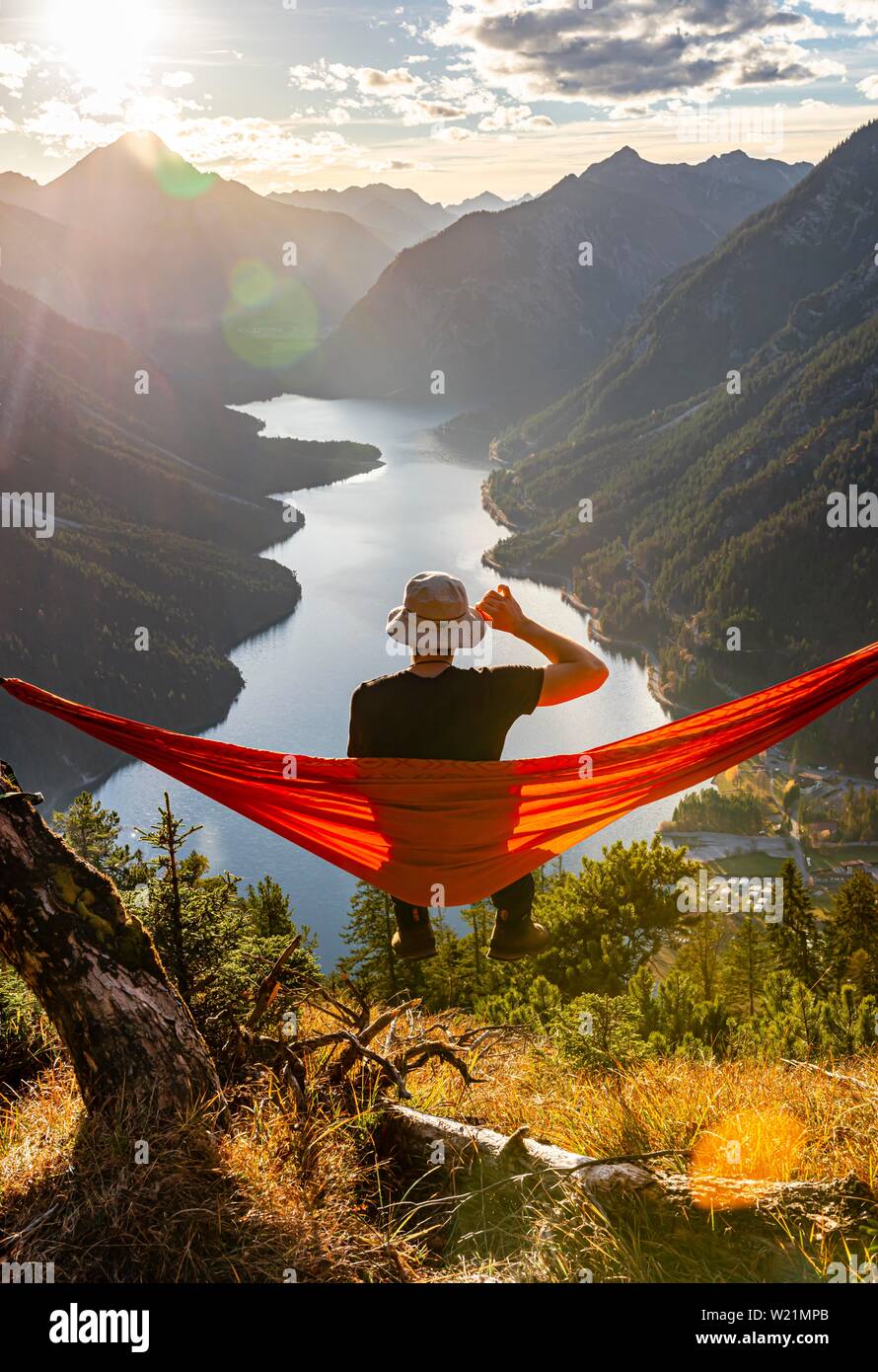 Mann mit einem Sonnenhut in einem orange Hängematte sitzen, Panoramablick  auf Berge mit See, Plansee, Tirol, Österreich Stockfotografie - Alamy