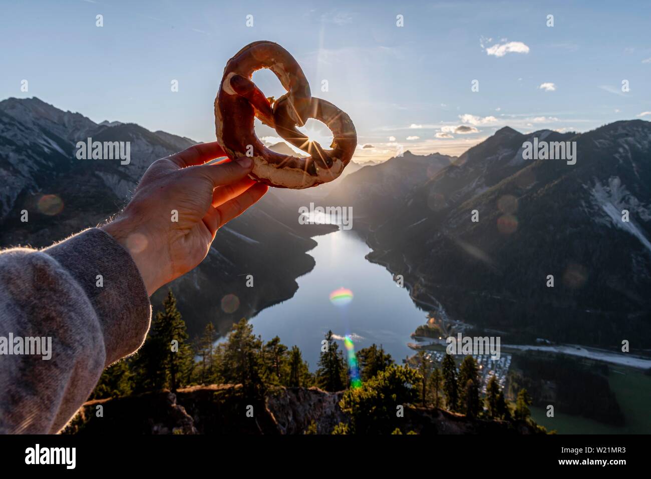 Hand, die Bayerische brezel vor Alpenpanorama Blick von Schonjochl, Plansee, Tirol, Österreich Stockfoto