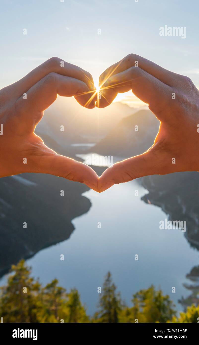 Hand bildet ein Herz vor der Alpen und Bergsee, Sun Star, Symbol der Liebe für die Natur und Wandern, Ansicht von Schonjochl, Plansee, Tirol, Österreich Stockfoto