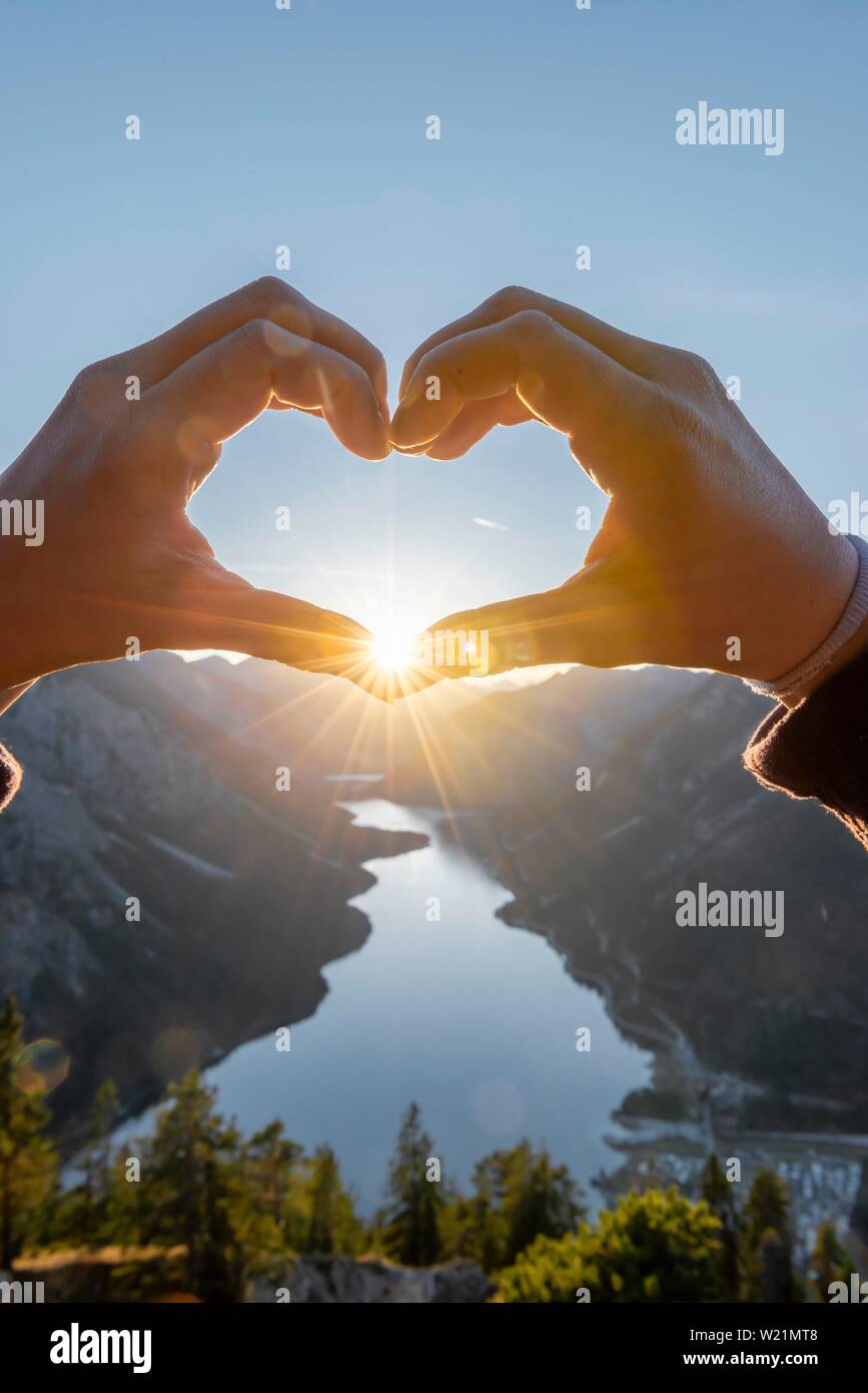 Hand bildet ein Herz vor der Alpen und Bergsee, Sun Star, Symbol der Liebe für die Natur und Wandern, Ansicht von Schonjochl, Plansee, Tirol, Österreich Stockfoto