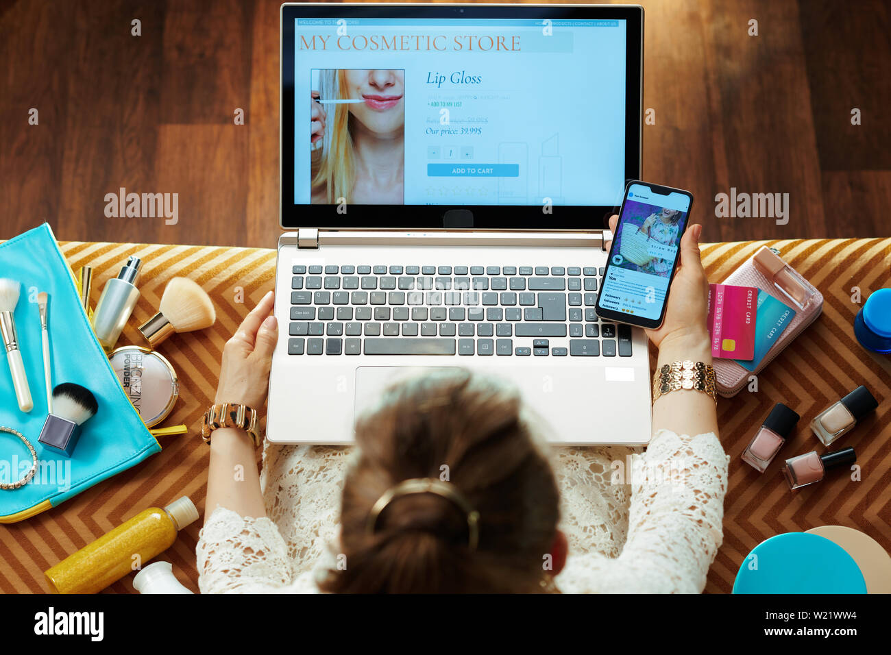 Obere Ansicht der modernen Frau in weißem Kleid mit Beauty Kosmetik online store auf einem Laptop und Smartphone mit e-Commerce social media Post whil Stockfoto