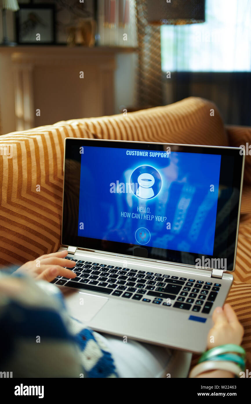 Frau auf der Couch im modernen Haus im sonnigen heißen Sommertag Aufruf robotic Kunden Service auf einem Laptop. Stockfoto